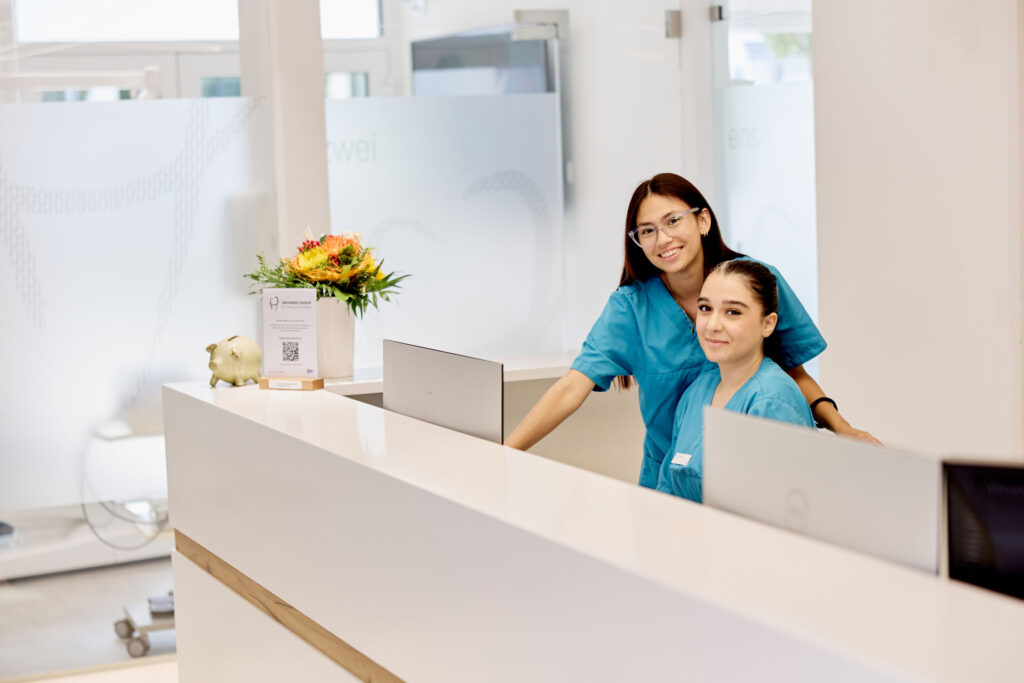 Zwei Mitarbeiterinnen begrüßen Patienten am Empfang der Praxis